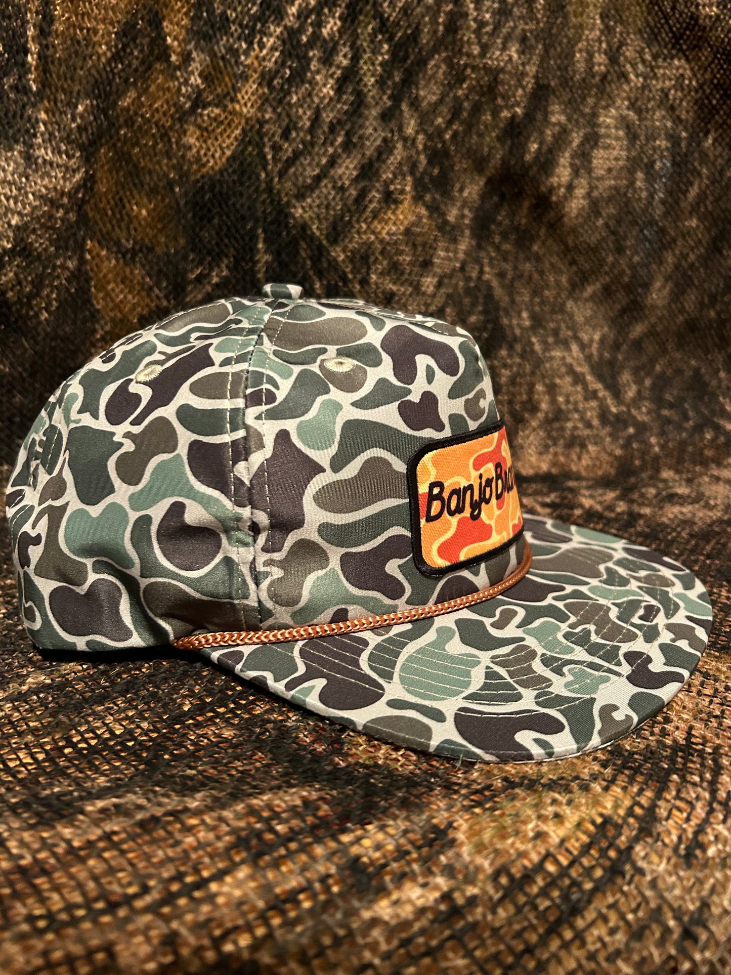 Banjo Brand script patch on a jungle Camo rope brim SnapBack hat