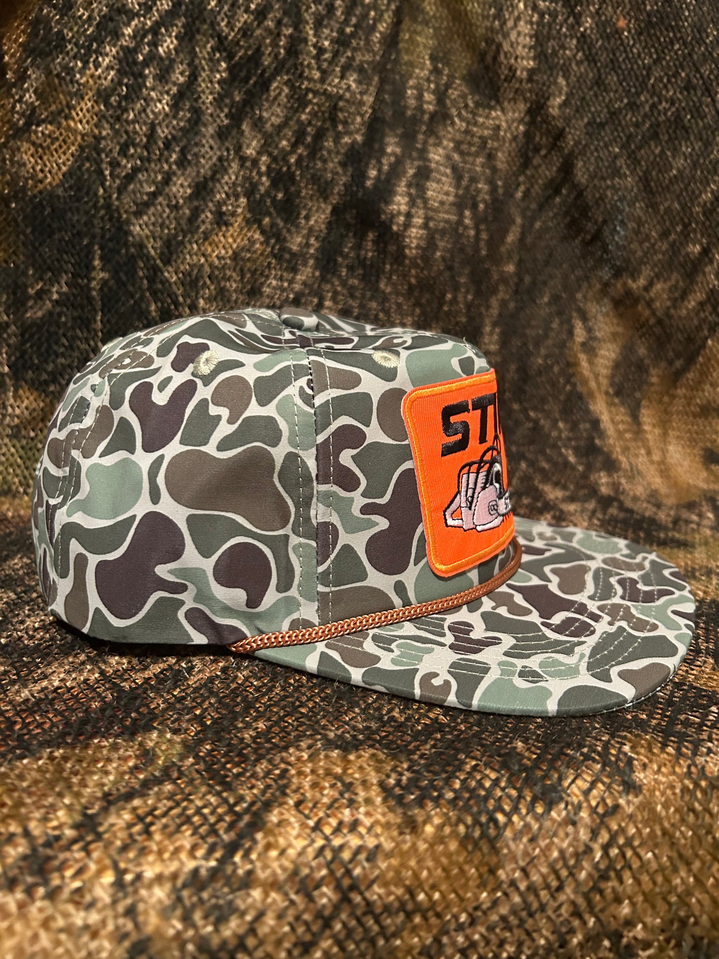 STIHL chainsaw patch on a jungle Camo ropebrim SnapBack hat
