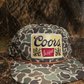 Coors gold patch on a green camo SnapBack hat