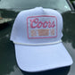 Coors Banquet pink patch on a white trucker hat